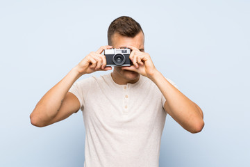 Young handsome blonde man over isolated blue background holding a camera