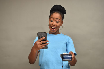 Fototapeta premium beautiful african lady holding a mobile point of sale device smiling and using her mobile phone