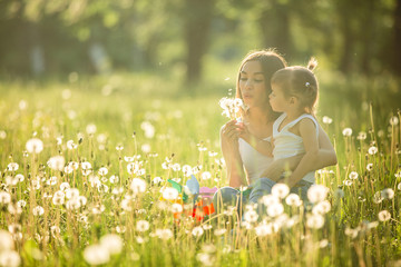 Portrait of happy mother and her little child on spring background. Cheerful family at dandelion...