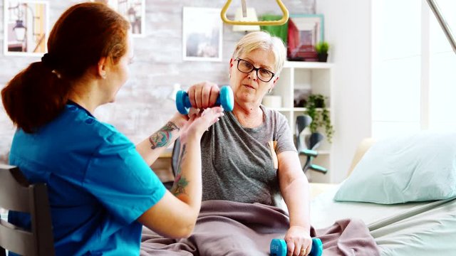 Nurse in retirement home helping an elderly woman to recover her muscle strength