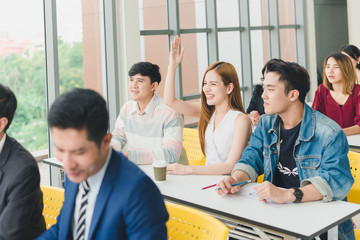 Asian male speaker is speaking at seminars and workshops to the people in the meeting. Those attending the meeting raised their hands to ask questions.