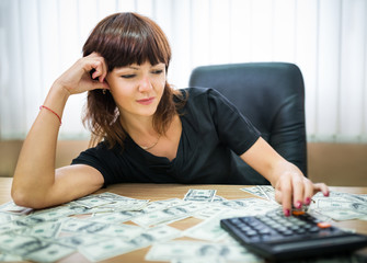 Happy young businesswoman counts her income in office