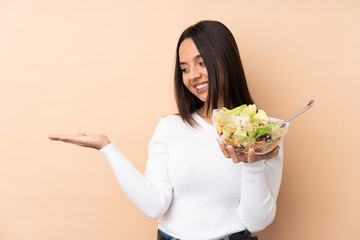Young brunette girl holding a salad over isolated background holding copyspace imaginary on the...