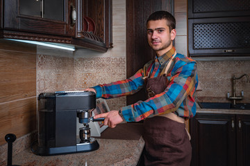 A stylish young man with beard,wearing casual clothes,cooks coffee in a coffee machine.