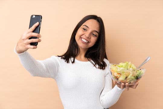 Young brunette girl holding a salad over isolated background making a selfie