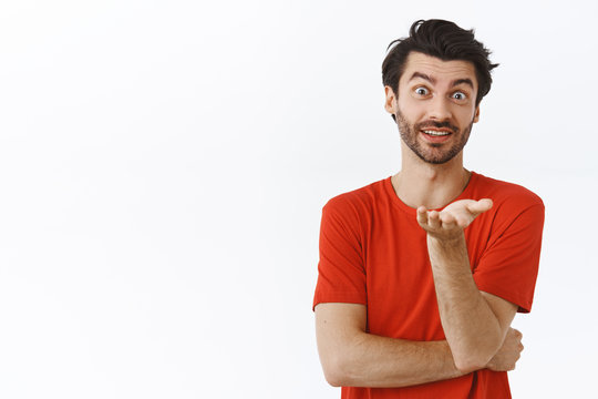 Guy discussing new tv serious, talking casually, asking your opinion as pointing camera with palm, standing happily over white background in red t-shirt, having conversation, white background