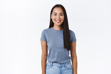 Obraz premium Portrait cheerful smiling asian woman with long dark hair, wear t-shirt and jeans, grinning joyfully, casual pose with arms down, express joy, carefree, relaxed emotions, standing white background