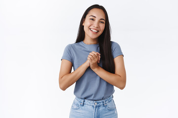 Happy, pleased charming asian woman clasp hands touched, receive help and thanking dearly, smiling joyfully, express gratitude and happiness, standing white background grateful