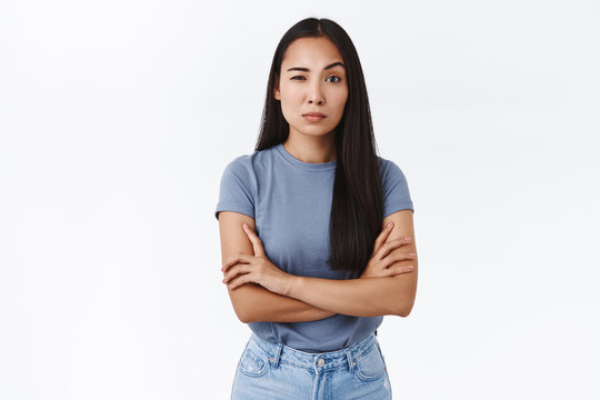 Skeptical and doubting young asian woman cross hands over chest in bossy, professional pose, stare judgemental and hesitant as measuring your ability cope with work, raise one eyebrow unsure