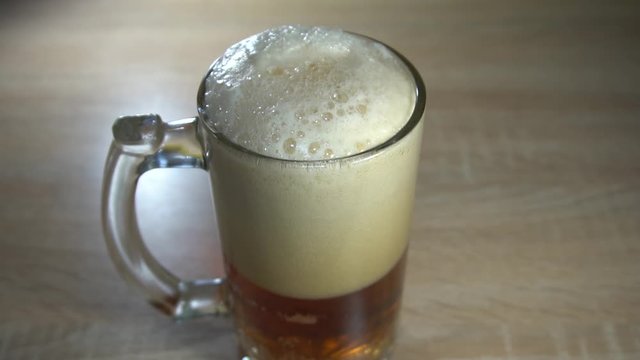 Thick foamy bubbles on fresh craft beer poured into a tall glass goblet with a handle. Slow motion video