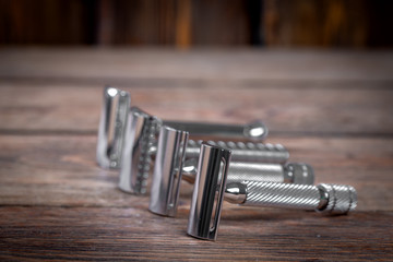 Metallic safety razors on rustic wooden boards background, barber shop concept