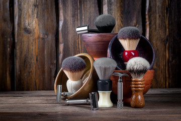 Metallic safety razors and shaving brushes with decorative bowls for shaving foam on rustic wooden boards background, barber shop concept