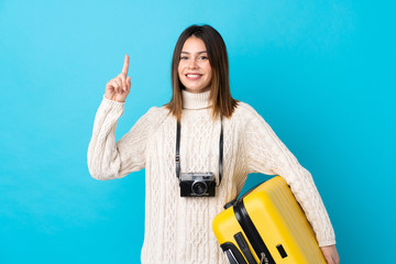 Traveler woman holding a suitcase over isolated blue wall intending to realizes the solution while lifting a finger up