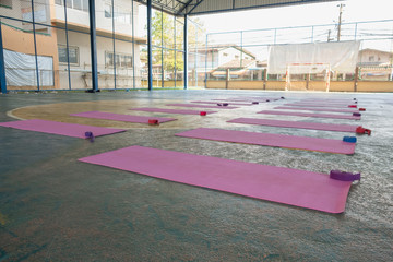 The pink yoga mat has a purple rope on top. The carpet is laid on the green concrete floor.