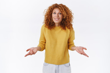 Indesicive, unsure cute young modern redhead curly woman in yellow sweater, spread arms sideways unaware, shrugging and smiling as cant help, dont know answer and apologizing for it