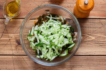 Step by step preparation of salad with seaweed, squid and pumpkin, step 5 - adding chopped fresh cucumbers to the salad, selective focus, horizontal