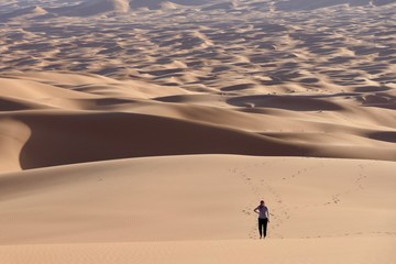 Fototapeta na wymiar Woman walking on sand dunes in Sahara, Morocco, Africa