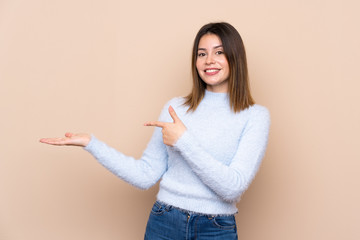 Young woman over isolated background holding copyspace imaginary on the palm to insert an ad
