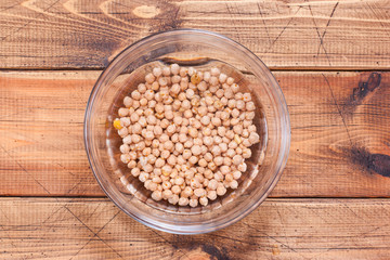 Dry chickpeas soaked in water in a glass bowl on a wooden table, top view, horizontal