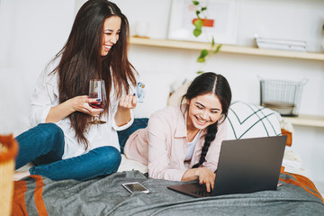 Young carefree brunette girls in casual with glass of wine buy online by credit card on laptop, shopping from home