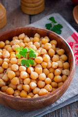 Boiled chickpeas in a wooden bowl on a wooden table, selective focus