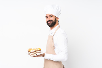 Young man holding muffin cake over isolated white background with arms crossed and looking forward