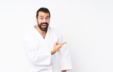 Young man doing karate over isolated white background surprised and pointing side