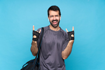 Young sport man with beard over isolated blue background making rock gesture