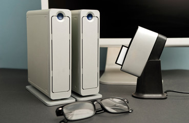 Conceptual work table photographer, composition, silver-colored desktop hard drive with lenses, compact flash card downloader, partial computer view, black background