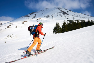 Male ski-climber climbing a snowy ridge in background the peaks of mountains at sunny day. Snow and winter activities, skitouring in mountains.
