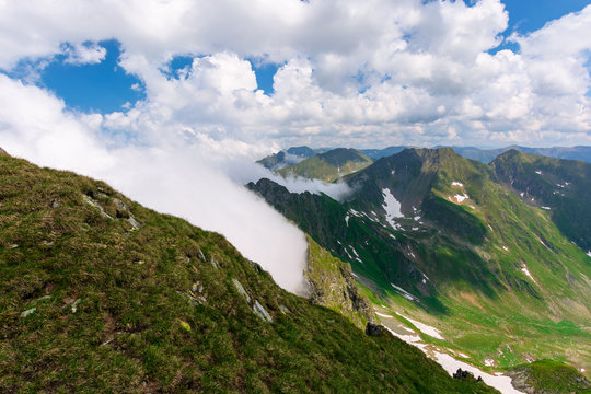 great summer scenery of high mountain range. steep slopes with rocks, grass and spots of snow. clouds on the blue sky. explore fagaras ridge of romania travel concept