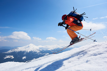 Fototapeta na wymiar Sportsman skier in skiing equipment jumping in air down steep snowy mountain slope on copy space background of blue sky and highland landscape. Winter risky sports, courage and speed concept.