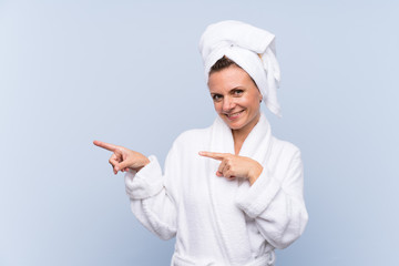 Woman in bathrobe over isolated blue background pointing finger to the side