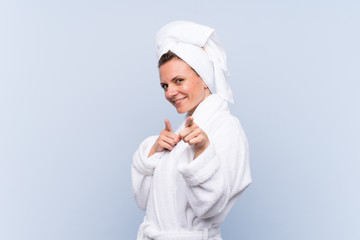Woman in bathrobe over isolated blue background points finger at you