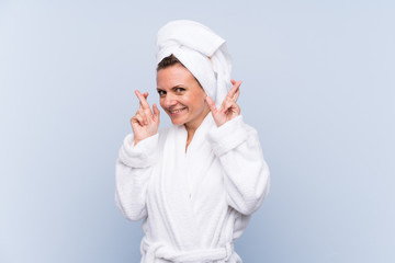 Woman in bathrobe over isolated blue background with fingers crossing