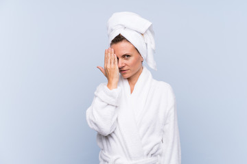 Woman in bathrobe over isolated blue background covering a eye by hand