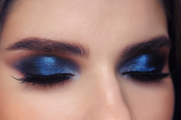 Closed eyes of young beautiful woman with gorgeous trendy facial makeup blue glossy eyelids