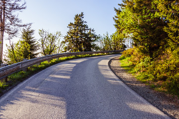 Mountain road between the trees with a blue sky on the background