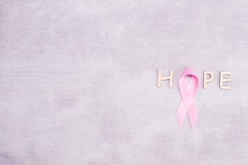 healthcare and medicine concept - pink breast cancer awareness ribbon and letters of the word HOPE on a gray background with place for text