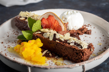 Brownie chocolate dessert with a scoop of white ice cream, slices of mango and a slice of...