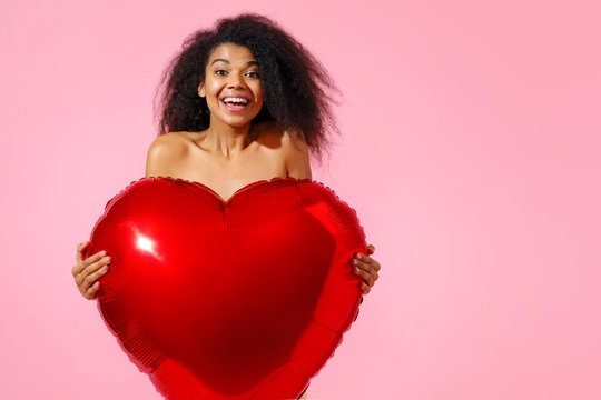 Happy girl holds red heart shape balloon. Photo of smiling young girl in love on pink background. Valentine's Day