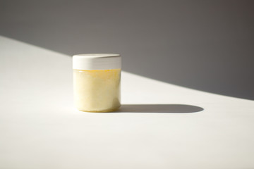 Jar with white cover and yellow scrub for body on white and grey background. Sun hard shadow from jar on background. Blank label for branding mock-up. Copy space. Cosmetic, beauty, spa and concept. 