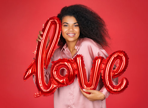 Cute girl hugs letter shaped balloon. Photo of smiling young girl in love on red background. Valentine's Day
