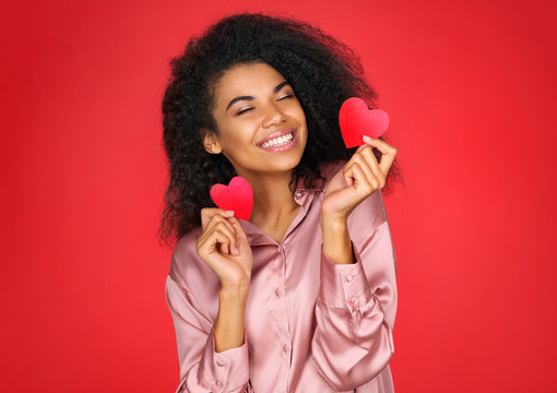 Happy girl holds red papers hearts and smiling. Photo of attractive latin girl in love on red background. Valentine's Day