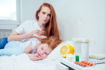 Obraz na płótnie Canvas redhaired ginger worried woman checking temperature of her sick little daughter