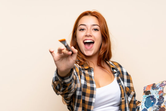 Teenager redhead girl holding a palette over isolated background