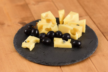 Cheese end black grapes on a slate plate on the wooden table