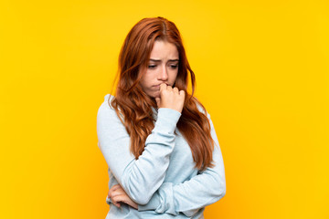 Teenager redhead girl over isolated yellow background having doubts