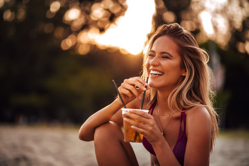 Close-up portrait of a beautiful happy young woman drinking on a beach. Summer vacation concept.