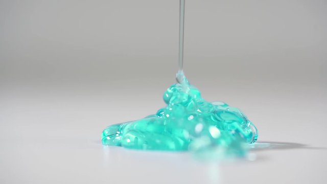 DETAILED: Turquoise gel pouring on white table and slowly lay down on the flatness. Light white studio room. 4-x slow motion, 100 fps to 25 fps video.
